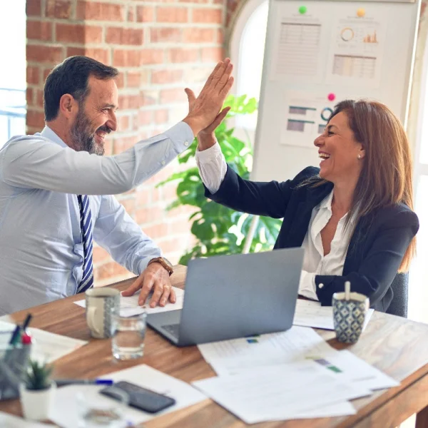 Two business professionals celebrate success with a high five at a desk, symbolizing teamwork in BPO services.