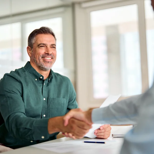 A man and another man shaking hands at a desk, symbolizing a successful B2B services partnership.