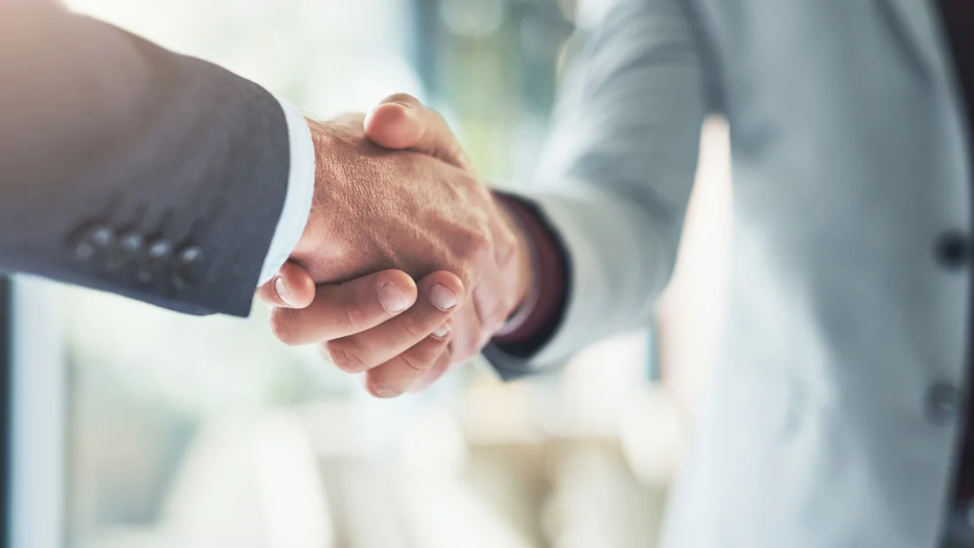 Two business professionals shaking hands in an office, symbolizing a successful B2B partnership.